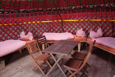 Interieur van een gezellige yurt met gestreept beddengoed en houten meubelen in Hofgut Hopfenburg, Baden-Württemberg.