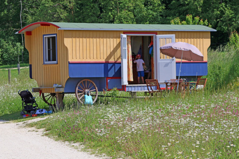 Glamping-overnatning med farverig zigeuner-vogn, udendørs siddeplads og børn i naturen hos Hofgut Hopfenburg.