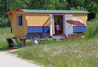 Glamping at Hofgut Hopfenburg: colorful gypsy wagon with outdoor table and children, wildflower setting.