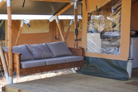 Outdoor glamping lodge tent with a wooden swing couch at Little Canvas Escape, Ameland campground.