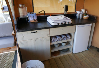 Kleine Küchenzeile im Glamping-Zelt Little Canvas Escape Ameland mit Herd, Kühlschrank und Regal.