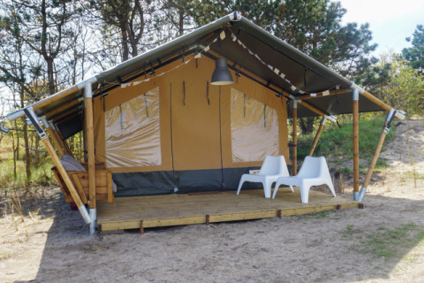 Alloggio glamping Little Canvas Escape - Lodgetenten Ameland con veranda e due sedie bianche all’aperto.