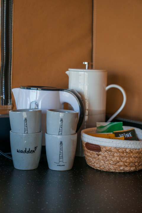 Krus, elkedel, kaffekande og kurv med te og kaffe på bord i luksustelt hos Little Canvas Escape Ameland.