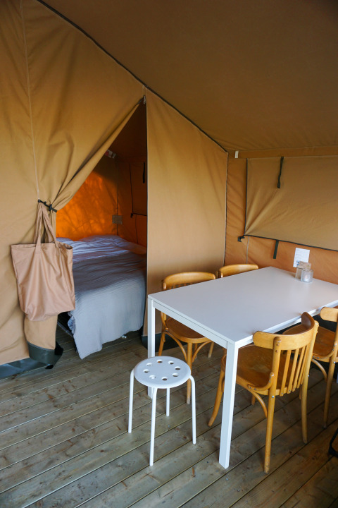 Interieur van een glamping tent met slaapgedeelte, eettafel en stoelen op houten vloer op Ameland.