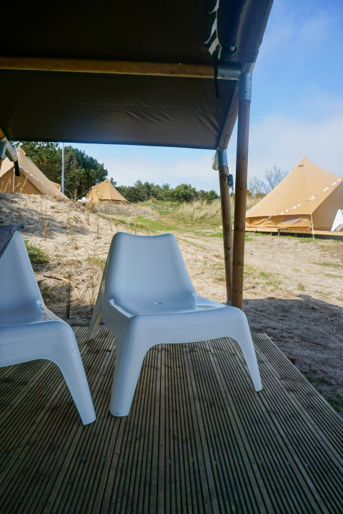 Blick von der Terrasse mit weißen Stühlen bei Little Canvas Escape - Lodgetenten Ameland, Glamping.