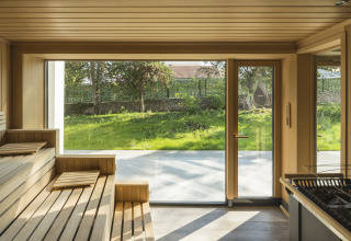 Interior de sauna con bancos de madera y grandes ventanales con vistas al jardín en Falkenstein Premium Camping Zadar.