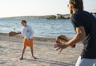 Boy and adult playing beach paddle tennis by the sea at Falkenstein Premium Camping Zadar - Mobile Homes in Dalmatia.