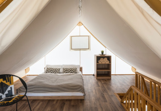Interior view of a luxurious glamping tent with a double bed, wooden flooring, and modern furnishings.