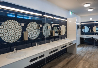 Modern sanitair op Falkenstein Premium Camping Zadar met meerdere wastafels en ronde decoratieve spiegels.