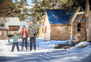 Familie macht Langlauf vor Holzchalets bei Huttopia Winter Chalets, La Clarée, in den französischen Alpen.