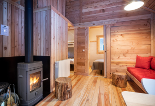 Indvendig af en hyggelig træhytte med brændeovn, stubbe som borde og rød sofa i Huttopia Winter Chalets.