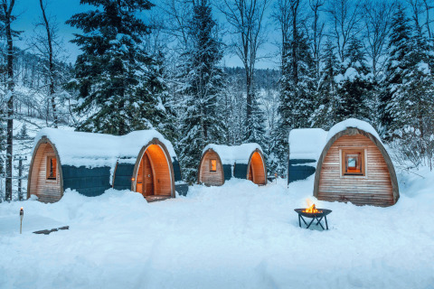 Verschneite PODhouses und Lagerfeuer in winterlicher Waldlandschaft bei Glamping Atzmännig - PODhouses & Lodges See-Gaster.