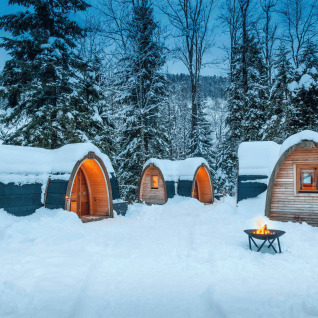 Snow-covered glamping PODhouses and firepit among trees at Glamping Atzmännig - PODhouses & Lodges See-Gaster.