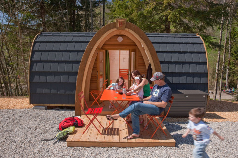 Family relaxes outside a pod-style cabin at Glamping Atzmännig - PODhouses & Lodges, surrounded by trees.