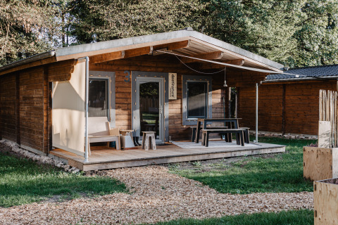 Accogliente chalet in legno al Destinature Dorf Südeifel, veranda con posti a sedere e area verde circostante.