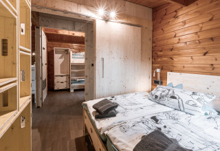 Slaapkamer in glamping verblijf Destinature Dorf Südeifel - Chalets Eifel met houten wand en tweepersoonsbed.