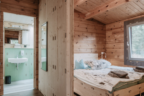 Vue intérieure d’un chalet glamping en bois avec chambre et salle de bain à Destinature Dorf Südeifel.