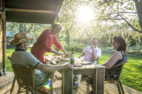 Cuatro adultos disfrutan de una comida al aire libre en Voedselbron Graauw - Safaritenten Zeeland, en un entorno natural.