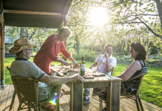 Quattro adulti gustano una cena all'aperto al glamping Voedselbron Graauw - Safaritenten Zeeland, immersi nel verde.