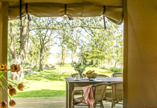 View from a safari tent to an outdoor dining table and lush greenery at Voedselbron Graauw in Zeeland.