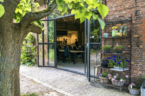 Ingresso del glamping Voedselbron Graauw con porte aperte, vista sul giardino e scaffale di fiori.