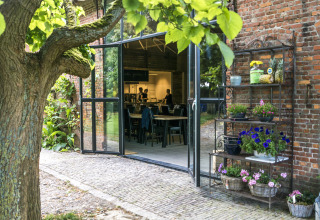Entrance to Voedselbron Graauw glamping with open doors, garden view, and shelves of flowers and fruit.
