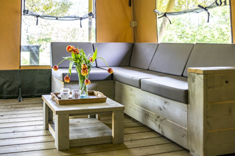 Innenaufnahme von Voedselbron Graauw - Safaritenten Zeeland mit Ecksofa, Couchtisch und Blumen.