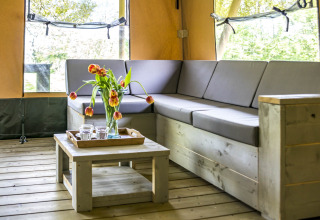 Vue intérieure de Voedselbron Graauw - Safaritenten Zeeland avec canapé d’angle, table basse et fleurs.