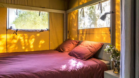 Alojamiento glamping en Safaritenten Zeeland con cama doble, luz natural y vistas al exterior desde las ventanas.