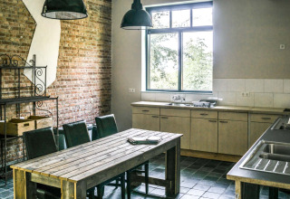 Fælles køkkenområde i Voedselbron Graauw - Safaritenten Zeeland med træbord, stole og stort vindue.