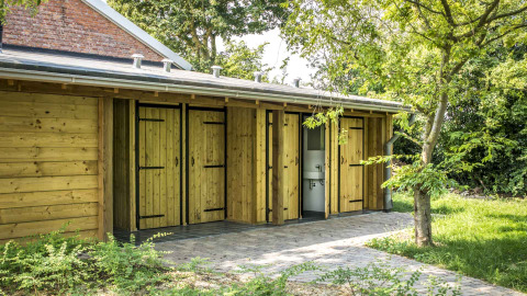 Außenansicht der Sanitäranlagen mit Holztüren bei Voedselbron Graauw - Safaritenten Zeeland Glamping.