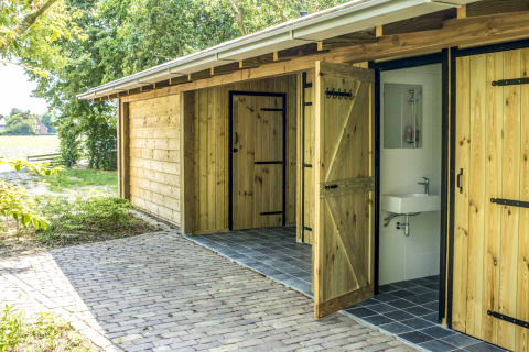 Edificio in legno all’aperto con porte aperte, lavabo e specchio, parte del glamping Voedselbron Graauw.