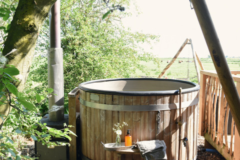 Buiten houten hottub bij Smûk Recreatie - Lodgetenten Friesland, omgeven door pracht van natuur en weiden.