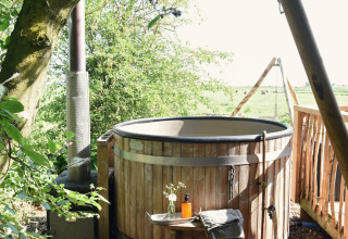 Outdoor wooden hot tub at Smûk Recreatie - Lodgetenten Friesland, surrounded by nature and field views.