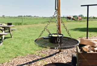 Outdoor hanging grill with pot and chains on a green field at Smûk Recreatie - Lodgetenten Friesland.