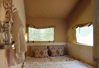 Intérieur d'une tente glamping chez Smûk Recreatie - Lodgetenten Friesland avec un lit douillet et fenêtres.
