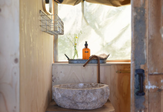 Rustic stone sink and copper faucet in wooden bathroom at Smûk Recreatie - Lodgetenten Friesland.