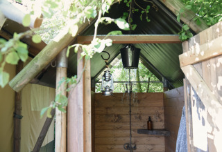 Ducha exterior en una tienda glamping de Smûk Recreatie en Frisia, rodeada de naturaleza verde.
