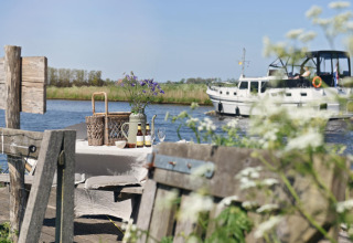 Glamping en Smûk Recreatie - Lodgetenten Friesland con mesa de picnic junto al agua y barco de fondo.