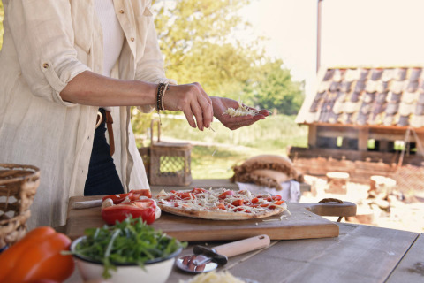 Person bereitet draußen Pizza zu bei Smûk Recreatie - Lodgetenten Friesland Glamping-Unterkunft.