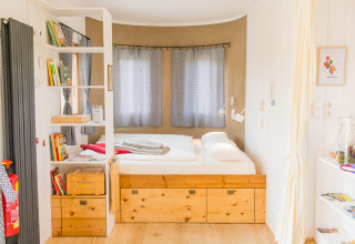 Loft glamping SONNENTOR lumineux et chaleureux en Autriche, lit intégré, étagères bois, grandes fenêtres.