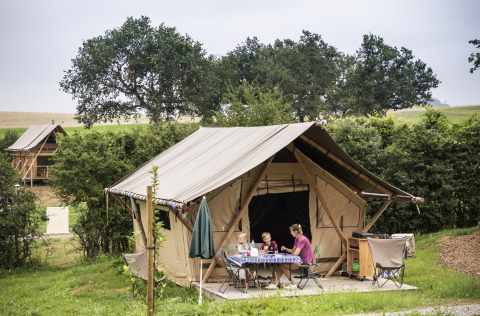 Familie entspannt vor einem Glamping-Zelt bei Camping Huttopia Pays de Cordes Sur Ciel in Occitanie.
