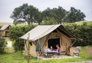 Family enjoys outdoor meal in front of luxury tent at Camping Huttopia Pays de Cordes Sur Ciel, Glamping Occitanie.
