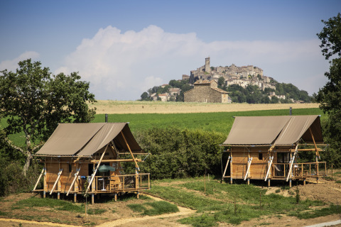 Dos tiendas de glamping en Camping Huttopia Pays de Cordes Sur Ciel, Occitania, con vista a un pueblo en la colina.