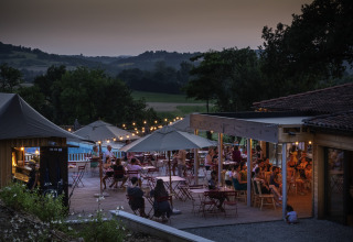 Terraza al aire libre al atardecer en Huttopia Pays de Cordes Sur Ciel Glamping, personas cenando.
