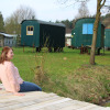 Woman sitting on wooden deck at Camping Böhmeschlucht with green pipowagens in the background in Lower Saxony.
