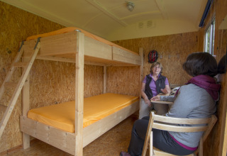 Due donne conversano all’interno di un’accogliente roulotte glamping con letti a castello in legno.