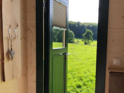 Vista da un Pipowagen presso Ferienhof Jeiler in Renania Settentrionale-Vestfalia, campi verdi da porta aperta.