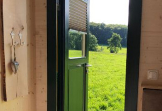 Uitzicht vanuit een Pipowagen bij Ferienhof Jeiler in Noordrijn-Westfalen, groene velden door open deur.