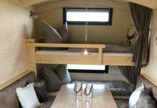 Innenansicht der Glamping-Unterkunft Ferienhof Jeiler - Pipowagen Nordrhein-Westfalen mit Bett und Sitzgruppe.